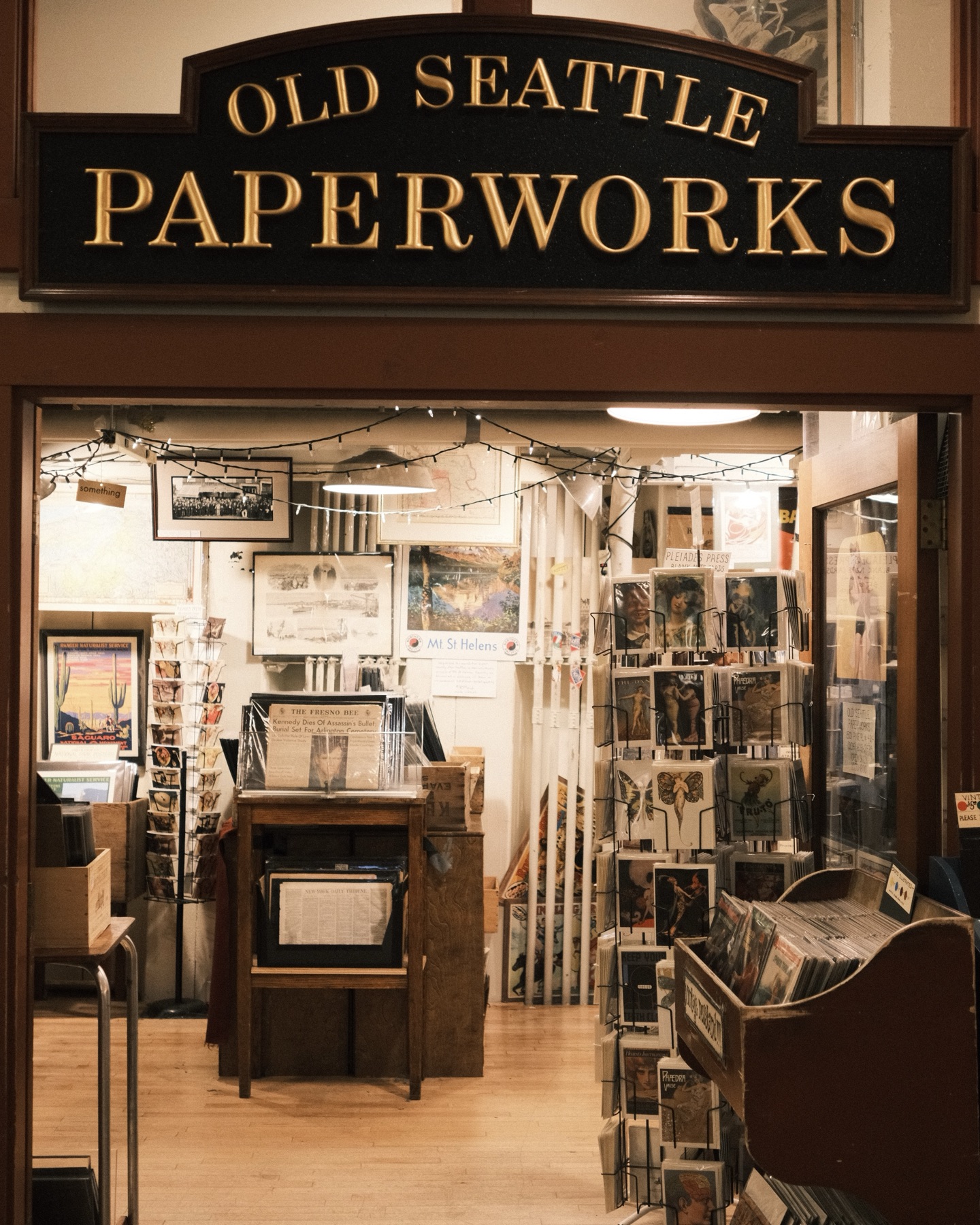 The warmly lit storefront of Old Seattle Paperworks, racks of prints inside