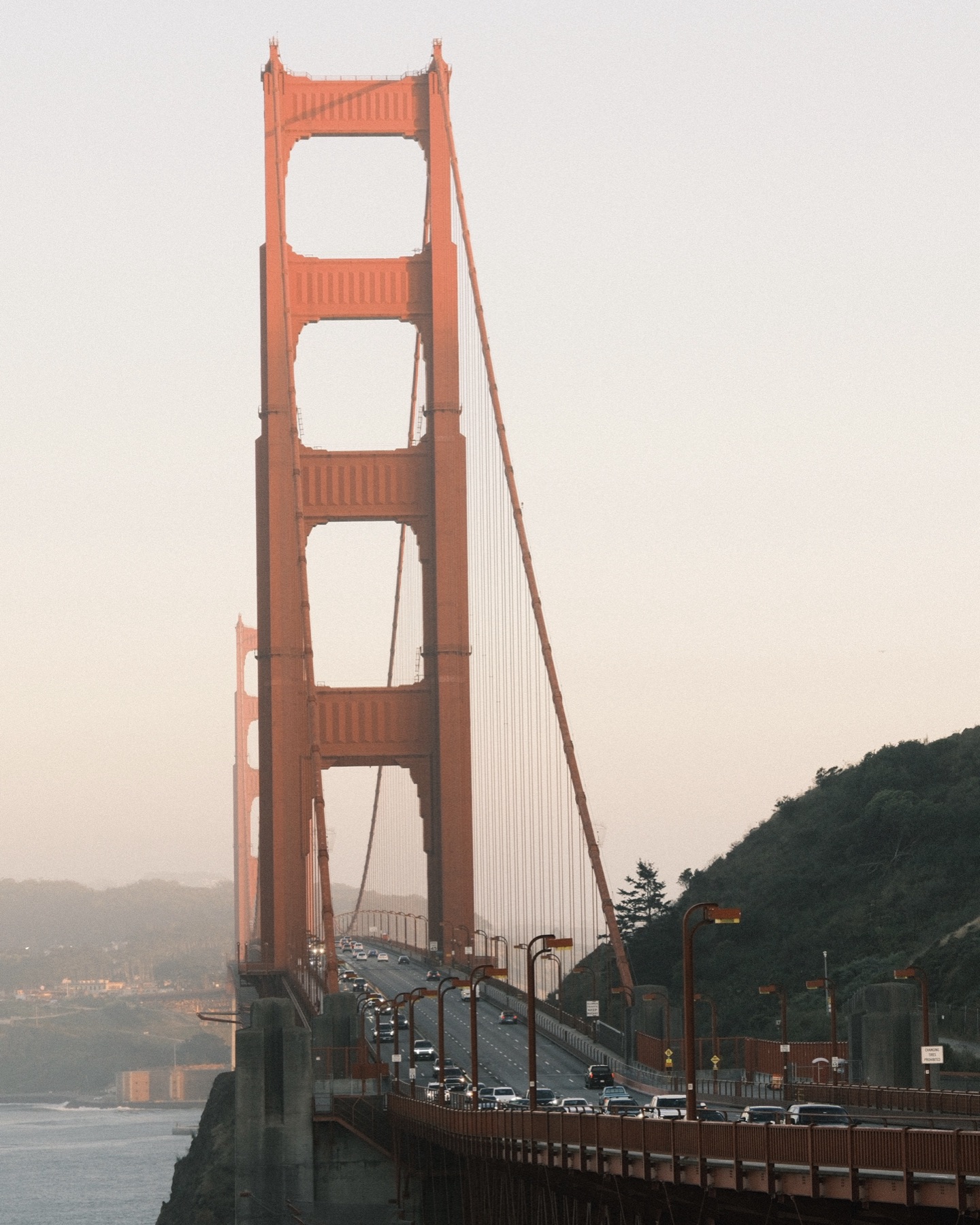 A tower of the Golden Gate Bridge in soft evening haze, traffic crossing below